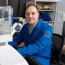 Man in blue lab coat beside white automated lab instrument in a lab
