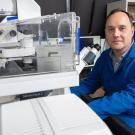 Researcher in a UC lab coat sits beside advanced microscope equipment, preparing for imaging work in the laboratory.